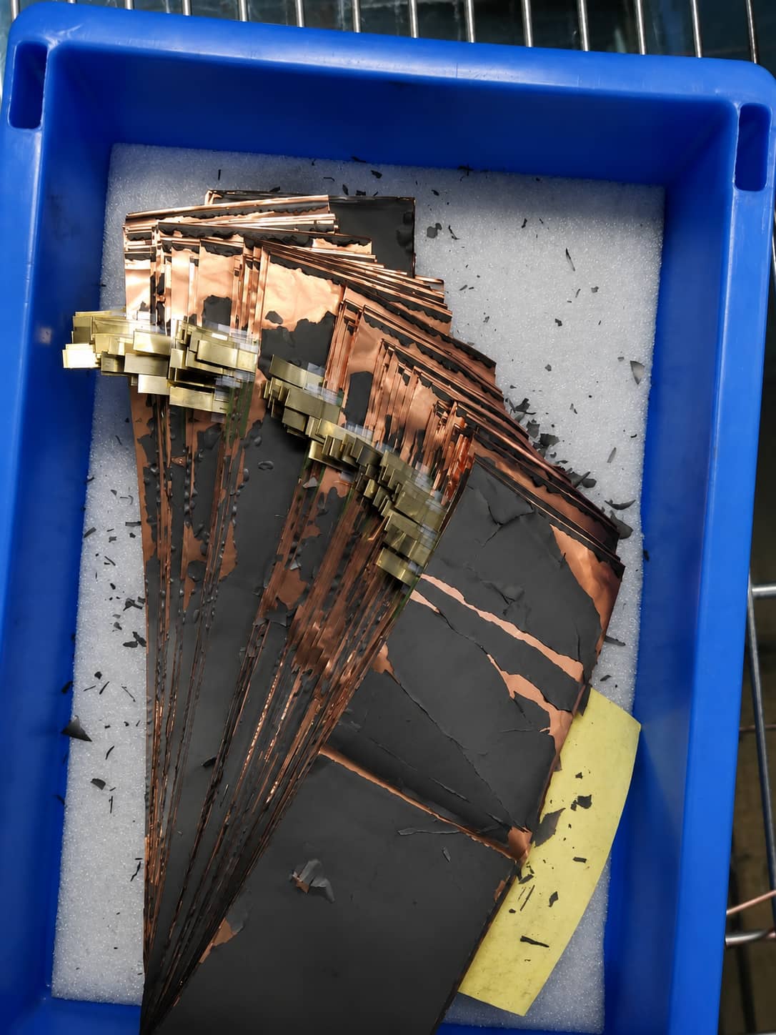 Severe electrode coating peeling and powder shedding from copper foil observed in historical CANRD novel binder pilot-line trials.